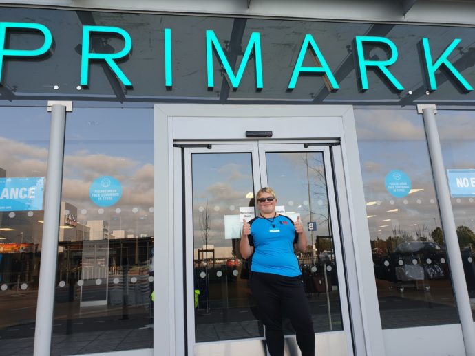 A person stood outside a Primark shop in a Primark uniform.